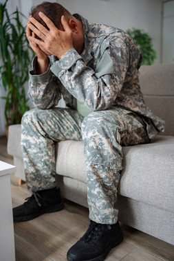 Kamuflaj üniformalı depresif asker koltukta el ele tutuşarak oturuyor.