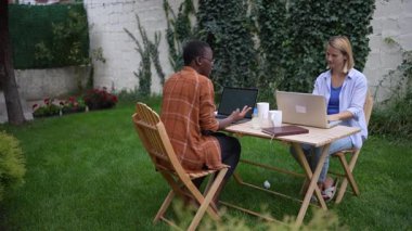 İki iş kadını bir bahçede dizüstü bilgisayarlar üzerinde çalışıyor, bir projeyi tartışıyorlar.