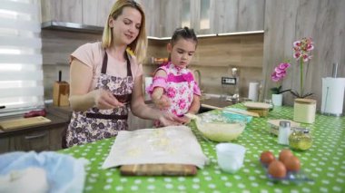 Mother and daughter sprinkling cheese on dough in the kitchen