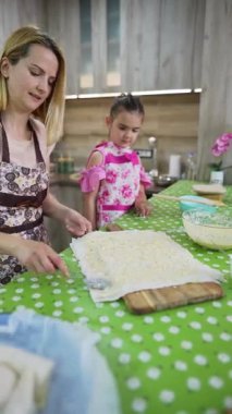 Mother spreading cheese filling on dough with her little daughter watching, preparing traditional homemade burek pastry