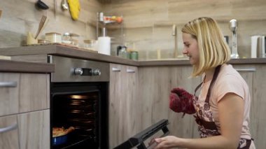 Young woman taking cooked pizza out of oven in kitchen
