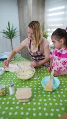 Mother and daughter spreading a dough for baking in the kitchen
