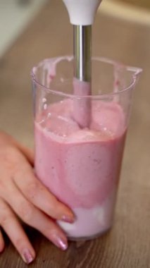 Immersion blender mixing pink ingredients in a transparent plastic container