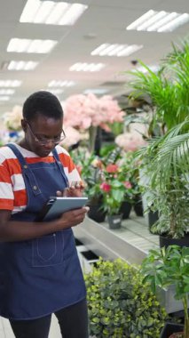 Young florist taking notes on her tablet and checking plants in a flower shop