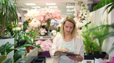 Florist writing notes on clipboard while checking plants in flower shop