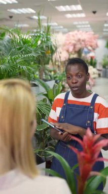 Florist using tablet, assisting customer choosing plants in a flower shop