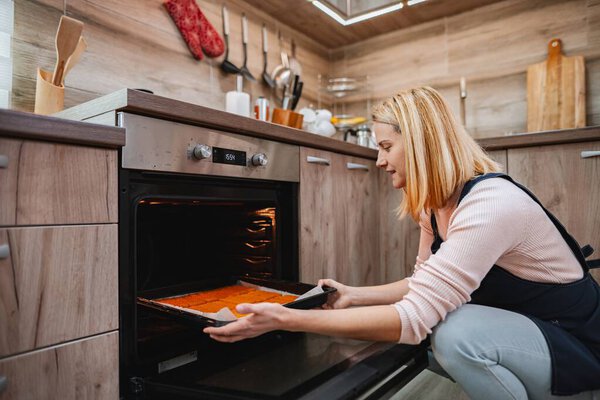Женщина аккуратно кладет поднос с выпечкой в теплую духовку.