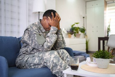 Mid adult military veteran experiencing emotional stress while sitting on a couch in a modern living room