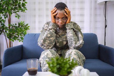 Depressed african american soldier suffering from ptsd sitting on sofa at home