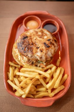 Taze malzemelerle süslenmiş lezzetli bir hamburger, yanında altın kızartmalar ve soslar, mükemmel bir yemek anı yaratıyor..