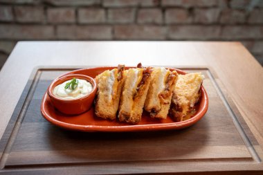 Ağız sulandıran ızgara peynirli sandviçler sade bir tabakta, yanında da kremalı bir sos. Sıcak yemek deneyimi için mükemmel..