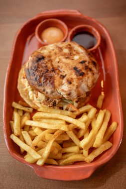 A warm, grilled chicken sandwich sits atop a plate accompanied by golden fries and two dipping sauces, inviting a delicious culinary experience.