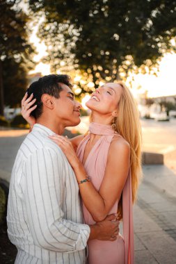 A couple shares a joyful moment under the glow of a setting sun, surrounded by nature.
