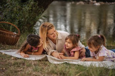 Happy mother having fun with her three daughters at a picnic by the river
