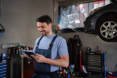 Smiling mechanic using a digital tablet while examining a lifted car in a repair shop