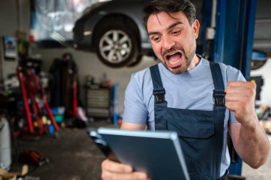 Mechanic looking at digital tablet and celebrating success in his auto repair shop