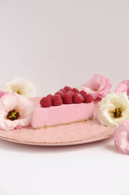 Ahudududulu cheesecake, taze çiçekli fotoğraf, pembe kek, beyaz arka plan konsept yiyecek sanatı tabağında böğürtlenli pasta.