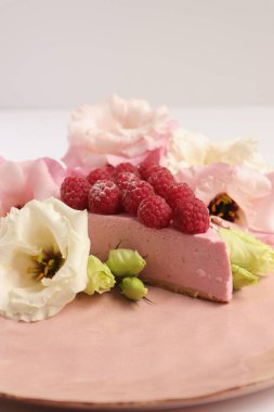 Ahudududulu cheesecake, taze çiçekli fotoğraf, pembe kek, beyaz arka plan konsept yiyecek sanatı tabağında böğürtlenli pasta.