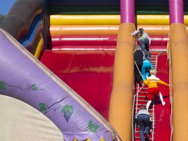 Çocuk bir şişme slayt tırmanmak. Yetişkin onları izliyor.