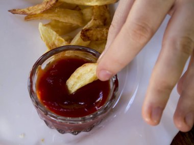 Beyaz renk, kızarmış patates kızartması, sosu, yeşil fışkın maydanoz bir tabağa. Bir kadın eli soslu patates ıslatma olduğunu. Ön biraz bulanık.