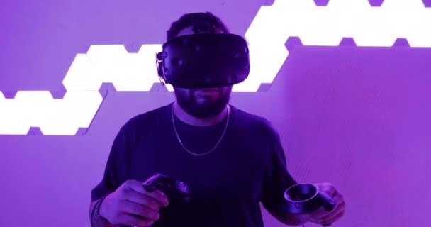 Muž v helmě virtuální reality tančí a hraje hry. Pokoj s neonovými světly. Video s efektem zrna, šum. — Stock video