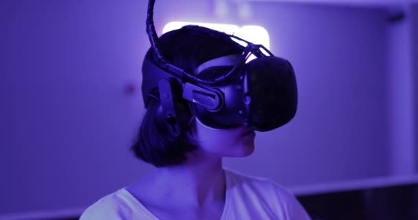 Kız neon bir odada VR gözlüğü takıyor. Bir kadın sanal gerçekliğe katılır. — Stok video
