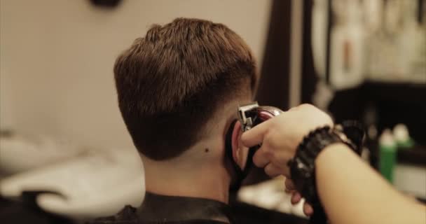 O barbeiro faz um corte de cabelo na barbearia com um cortador de cabelo . — Vídeo de Stock