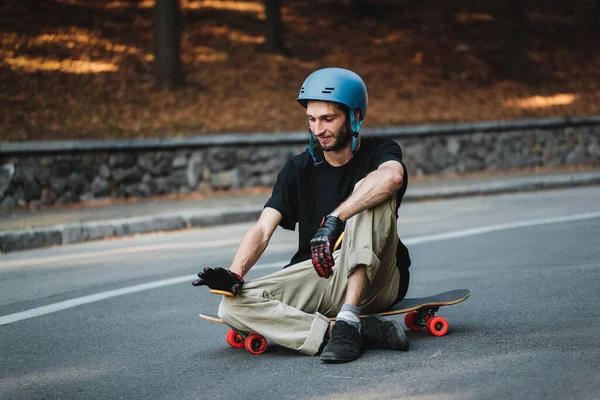 Der Kerl sitzt auf einem Holzbrett. Ruhe nach dem Skateboarden. — Stockfoto