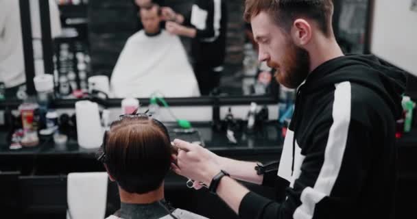 Cabeleireiro com barba faz um corte de cabelo ao cliente . — Vídeo de Stock