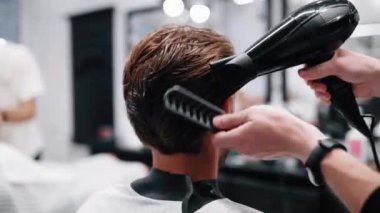 Berber saçını kurutmak için saç kurutma makinesi kullanıyor..