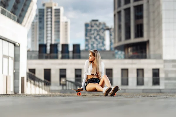 Mulher bonita sentada em um longboard. Cidade grande da noite. — Fotografia de Stock