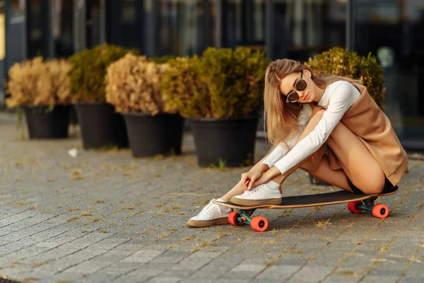 Kvinna med glasögon sittande på en skateboard. Livsstil i staden. — Stockfoto