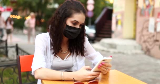 Een jonge vrouw met een zwart masker van het virus zit op straat. — Stockvideo