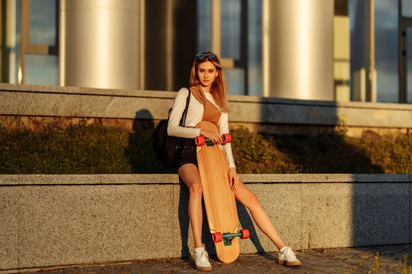 Bella giovane bionda con un longboard in mano al tramonto. — Foto Stock