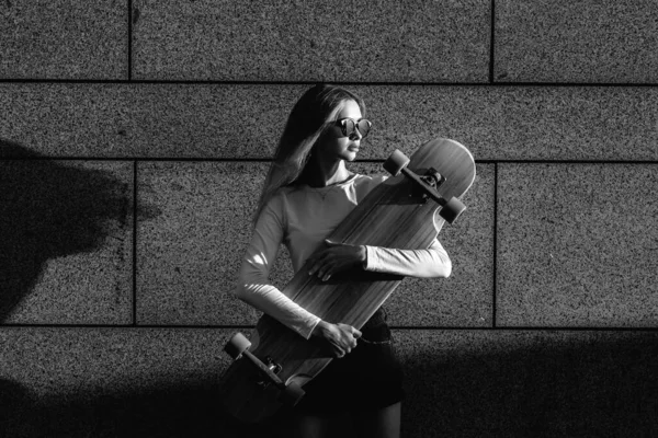 Steep black and white portrait of a young woman with a longboard in her hands. — Stock Photo, Image