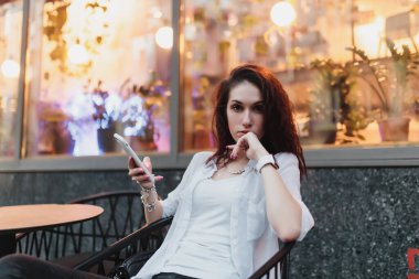 Genç bir kadın akşamleyin sokakta bir masada oturuyor..