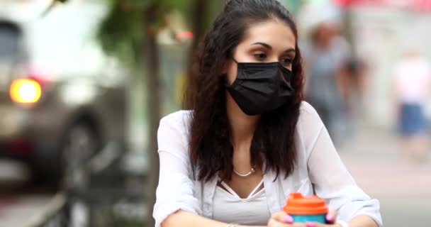 Young woman in a mask sitting on the street with coffee — Stock Video