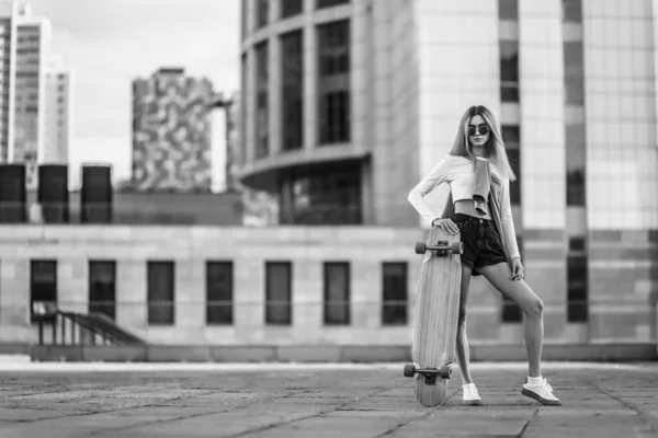 Ritratto in bianco e nero di una giovane donna seduta su uno skateboard — Foto Stock