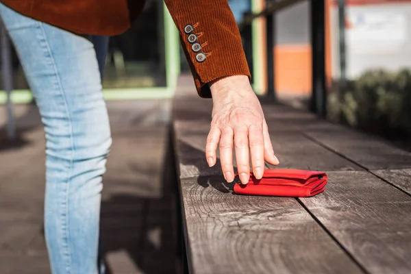 Woman picking up lost wallet from bench in city.  Female hand taking red leather wallet on street