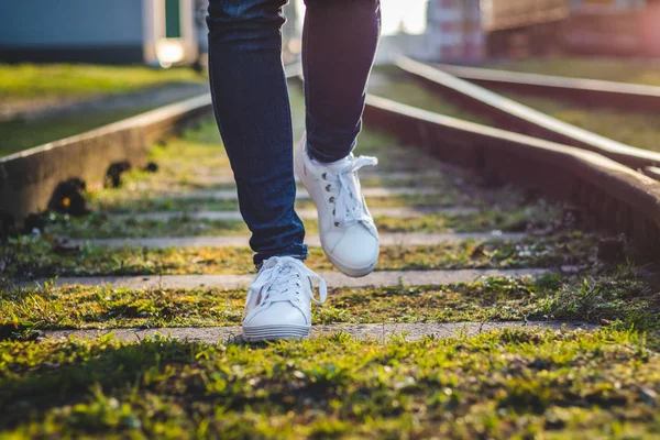 Woman wearing white sneakers running on railroad track. Female legs with sports shoe. Exercise outdoors.