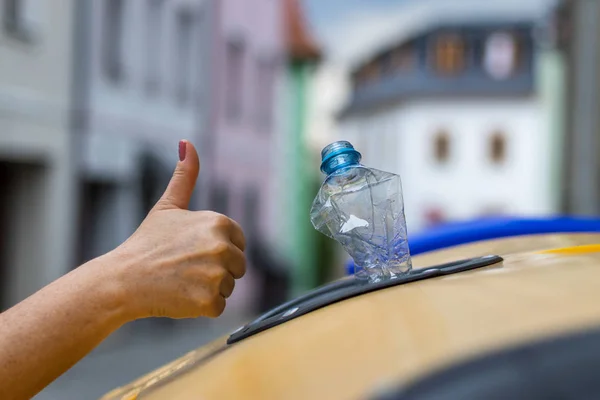 Plastik atıkların ve ayırma çöplerinin geri dönüşümü için başparmak. Çevre koruma. Geri dönüşüm kutusunda plastik şişe ve insan eli