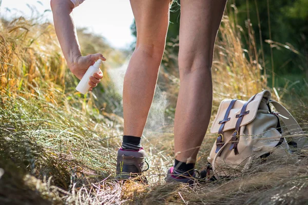 Hiker using mosquito repellent outdoors. Woman tourist applying insect repellent against tick and mosquito on her legs in nature