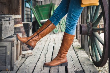 Deri çizme ve kot pantolon giyen kadın. Çiftlikte duran manken. Vahşi batı retro tarzı