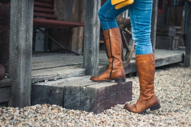 Kot pantolon ve deri çizme giyen ve çiftlikte ki ahşap merdivenlerde duran kadın. Binicilik botu giyen kadın bacakları