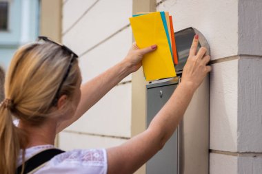 Posta çalışanı posta kutusuna mektup lar ekiyor. Kadın elinde renkli zarflar tutuyor. Yazışmaları teslim eden posta taşıyıcı