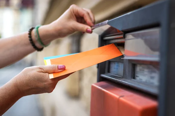 Sending letters by mail. Woman inserting envelope into public mailbox at post office. Female hand sending letter