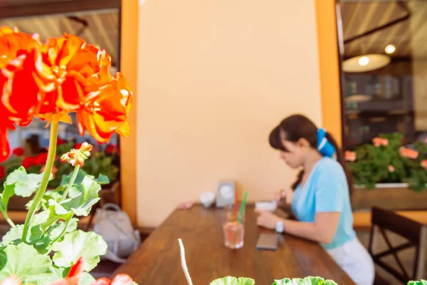 Woman drinking cool drinks in cafe. focus on flower in front. blurred background — Stock Photo, Image