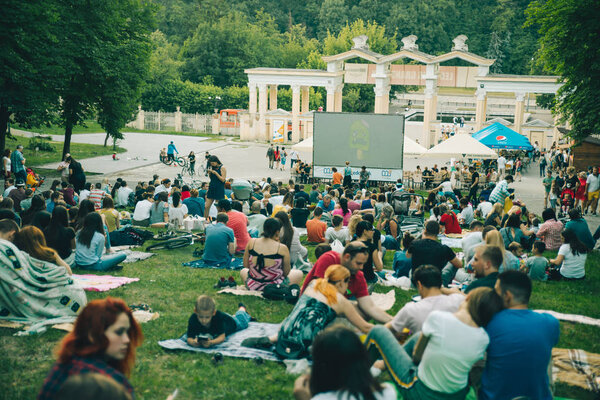 LVIV, UKRAINE - JUNE 1, 2018: people sitting on grass in city park watching movie in open air cinema