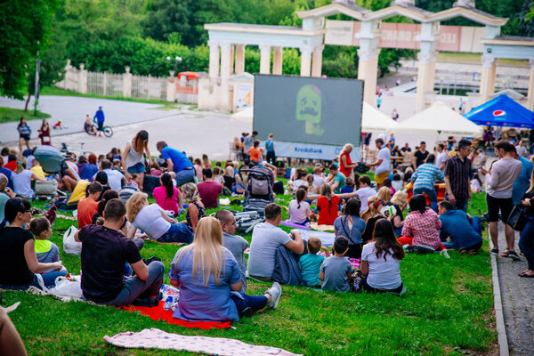LVIV, UKRAINE - JUNE 1, 2018: people sitting on grass in city park watching movie in open air cinema