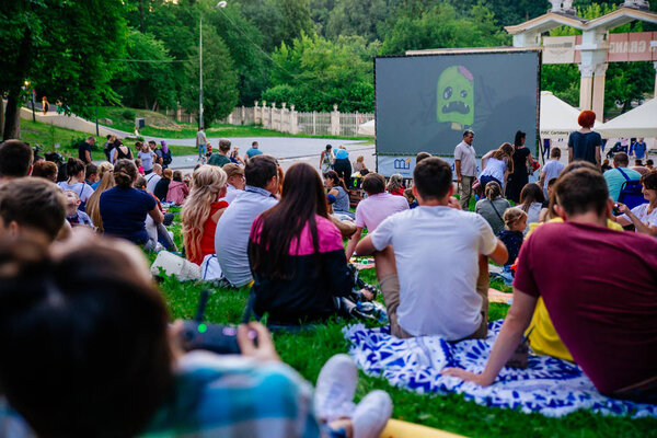 LVIV, UKRAINE - JUNE 1, 2018: people sitting on grass in city park watching movie in open air cinema